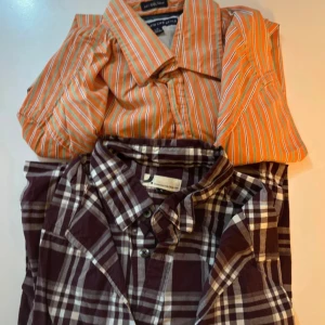 Två skjortor, randig orange & rutig vinröd - Säljer två skjortor i storlek L. En orange skjorta från New Life Style med vita och gröna ränder, klassisk krage och knäppning. Den andra är vinröd och vit-rutig från Dressmann, också med knappar och klassisk krage. Perfekta för dig som gillar färg och mönster.