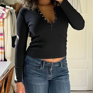 Svart ribbad långärmad topp från Zara - Svart långärmad topp från Zara med ribbad struktur och v-ringning med silvriga knappar. Modellen är figurnära men sitter inte obekvämt tajt