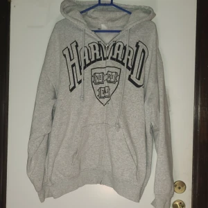 Grå Harvard hoodie med dragkedja S - Grå hoodie med stort Harvard-tryck på bröstet, huva med snörning och praktisk dragkedja framtill. Mjuk bomullsblandning och två fickor. Perfekt för chill dagar och pluggsessioner. Oversized känsla och klassisk college-vibe.