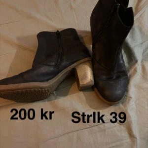 Svarta boots med klack, strl 39 - Snygga svarta boots med rund tå och grov klack. Skorna har dragkedja på sidan och är tillverkade i skinn med en robust sula i beige ton. Perfekta för dig som gillar stilrena och klassiska skor med lite höjd.