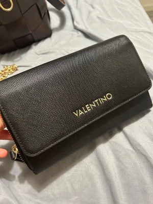 Svart axelväska från Mario Valentino - Snygg svart axelväska från Mario Valentino med guldfärgade detaljer och kedja. Väskan är tillverkad i strukturerat skinn och har ett stilrent, elegant utseende. Invändigt finns flera fack och kortplatser, perfekt både vardag och fest!💞💞