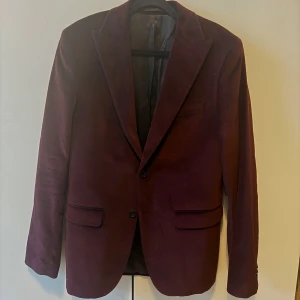 Vinröd Sammets Kavaj Från bläck - Säljer en vinröd kavaj från Bläck i mjuk manchester. Kavajen har skräddad passform, klassiska slag, två knappar framtill och fickor med lock. Perfekt för dig som vill sticka ut med en snygg färg och cool textur.