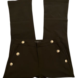 Svarta bootcut kostymbyxor med silverknappar - Svarta bootcut kostymbyxor från Calliope med snygga silverknappar framtill. Byxorna har hög midja och klassisk bootcut passform. Storlek Xs-S.