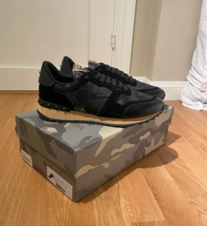 Valentino rockrunners - Snygga Valentino Garavani Rockrunner sneakers i svart med mörkgrått kamouflagemönster. Skorna har detaljer i mocka och skinn, samt ikoniska nitar på hälen. Beige sula och svarta snören. Kommer med originalkartong och extra skosnören. Helt nya, har äkthetscertifikat från Siciuro fashion som kan visas vid affär. Kom privat för mer frågor!