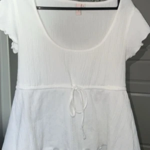 Vit kortärmad klänning med knytband - Söt vit klänning med korta ärmar och knytband i midjan. Perfekt för varma dagar med sin lätta och luftiga design. Den har en rund halsringning och ett enkelt, stilrent utseende.