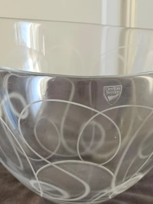 Orrefors Pond glasskål design Råman - Säljer en stilren glasskål från Orrefors, modell Pond designad av Ingegerd Råman. Skålen är transparent med vita slingrande linjer som ger en modern och clean vibe. Perfekt som centerpiece eller till snacks. Höjd 159 mm, diameter 218 mm. Kommer i originalkartong.