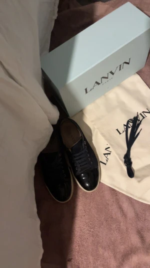 Lanvin skor Navy Mörkblå byte - Säljer ett par svarta sneakers från Lanvin med snygg glansig finish och vita sulor. Skorna har klassisk snörning och rund tå. Kommer med originalkartong och dustbag. Perfekta för dig som gillar stilrena och exklusiva sneakers. Byter! Priserna stämmer absolut inte till er som tror de 😙 dessa e Navy