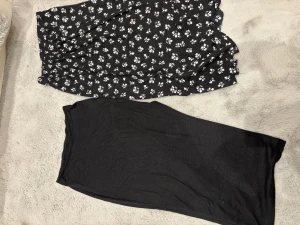 Två svarta kjolar, en blommig och en enkel - Säljer två  svarta kjolar i nya skick, Den ena är mönstrad med vita blommor och Den andra är helsvart med slits. Går att köpa separat och pris går att diskuteras.🥰🤍