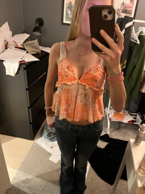 Blommig volang topp i orange färger - Supersöt linnetopp med blommigt mönster i orange och beige toner. Toppen har volangdetaljer, v-ringning och tunna axelband. Perfekt för sommarens varma dagar och ger en riktigt trendig vibe. Väldigt fin när man är brun