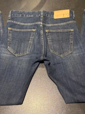 Tiger of Sweden jeans blå - Snygga mörkblå jeans från Tiger of Sweden, modell Freesixty Blu Killer Slight. Klassisk femficksdesign med kontrastsömmar och läderpatch bak i midjan. Jeansen har rak passform och är tillverkade i slitstarkt denim från Italien storlek 28/30