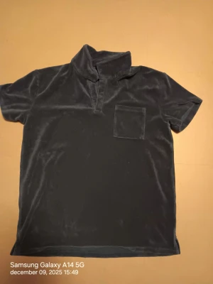 Mörkblå sammetstopp från Lindex - Säljer en mörkblå topp från Lindex i mjuk sammet. Modellen har korta ärmar, en hög krage med öppning framtill och en liten bröstficka. Perfekt för dig som gillar chill och stilren vibe. Färgen är djup och materialet känns lyxigt mot huden.