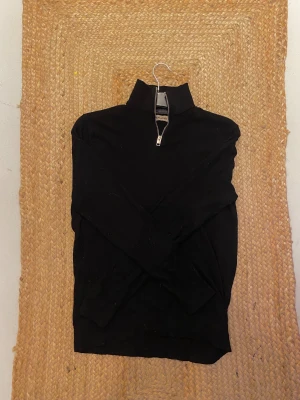 Svart half zip tröja Jack & Jones S - Svart långärmad tröja från Jack & Jones med hög krage och half zip-dragkedja framtill. Tröjan är i en klassisk, enkel modell och passar perfekt till lager-på-lager. Materialet är mjukt och bekvämt, perfekt för kyligare dagar.