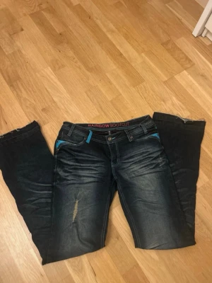 Bootcut jeans med blå läderdetaljer - Inte mina bilder! Snygga mörkblå bootcut jeans från Rainbow med blå läderdetaljer vid fickor och midja. Jeansen har dragkedjor på bakfickorna och låg midja. Jag köpte dem på vinted men dem passade inte så jag säljer dem vidare💞💞 det drog att tjejen jag köpte dem av hade gjort slitningarna på sista bilden själv💗stig att det var storlek S/36/8
