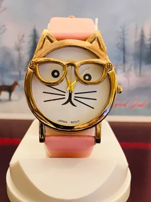 Charmig Damklocka med Kattmotiv  - Charmig Rosa/Guld dam klocka med kattmotiv och glasögon. Urtavlan har kattansikte med morrhår och texten "Japan Movt". Boetten är guldfärgad och armbandet är rosa.Rustad med nytt batteri, fungerar fint! Säljes i befintligt skick enligt bilderna.