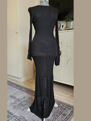 Svart lång stickad klänning - Svart långklänning med ribbad överdel och utsvängda ärmar. Nederdelen och ärmsluten har ett snyggt spetsstickat mönster. Klänningen har en slim passform och är tillverkad i stickat material som sitter snyggt och bekvämt.