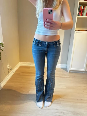 Coola lowwaist bootcut jeans med ringdetaljer - Coola snygga unika jeans i unik design. Jättesnygga till vardags och perfekta till temafest ex. Rock ’n’ roll tema. De är stretchiga i materialet  Midjemått: 38 cm  Innerben: 78 cm  Passar mig som är 165 cm lång Kolla min profil, finns massa liknande! 💞