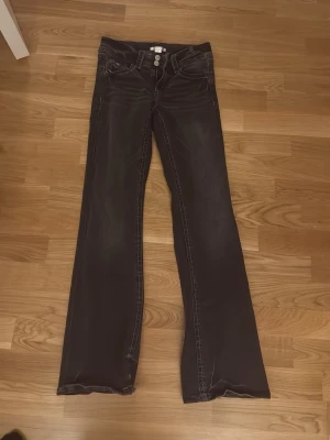 Svarta bootcut jeans Gina Tricot - Snygga svarta jeans från Gina Tricot i storlek 158. Modellen har bootcut-ben och två silverfärgade knappar framtill. Jeansen har klassisk femficksdesign och är tillverkade i jeansmaterial med kontrastsömmar.