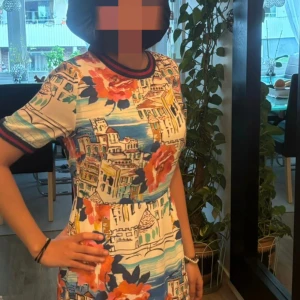 Färgglad Positano-klänning från Oui - Säljer en unik kortklänning från Oui med Positano-inspirerat mönster, stora blommor och stadsmotiv i blått, rött, orange och beige. Klänningen har korta ärmar, rund hals med randig ribbad kant och volang med leopardmönster längst ner. Perfekt för dig som gillar färg och detaljer!