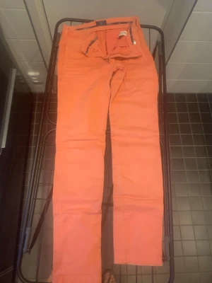 Orange chinos från Morris - Snygga orange chinos från Morris med klassisk rak passform. Byxorna har dragkedja, bälteshällor och detaljer med Morris-logga på insidan av midjan. Tillverkade i mjuk bomull som känns skön mot huden. Perfekt för dig som gillar färgstarka plagg.