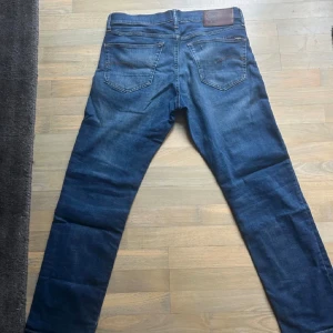 Blå jeans från G-Star RAW - Snygga blå jeans från G-Star RAW med klassisk femficksdesign och bruna detaljer på bakfickorna. Jeansen har en rak passform och är tillverkade i slitstarkt denim med lätt tvättad look. Perfekt för dig som gillar streetstyle och vill ha en cool vardagslook.