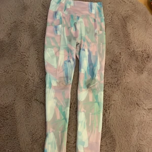 Färgglada leggings från SOC - Säljer ett par snygga leggings från SOC i storlek 134/140. De har ett färgstarkt abstrakt mönster i pastellfärger som rosa, blått och grönt. Tillverkade i ett stretchigt syntetmaterial som andas, perfekta för träning eller chill.