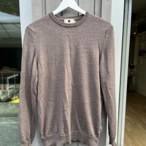 Brun ulltröja från NN07 - Säljer en stilren brun tröja från NN07 i 100% extrafin ull. Tröjan har rund halsringning, ribbade muddar och lång ärm. Perfekt för dig som gillar en klassisk och enkel look med premiumkänsla. Extra bra nu till hösten. Tveka inte att höra av er om frågor!