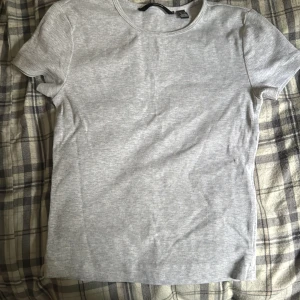 Ljusgrå ribbad t-shirt från Vero Moda - En stilren ljusgrå t-shirt från Vero Moda i ribbad bomull. Modellen är klassisk med rund halsringning och korta ärmar. Perfekt basic-plagg att matcha med allt. Snygg och enkel att bära till jeans eller kjol.