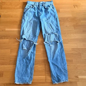 Ljusblå slitna jeans från Gina - Ljusblå jeans med raka ben och stora slitningar över båda knäna. Klassisk femficksmodell med hög midja och råa kanter nertill. Jeansen är i denim och har en avslappnad, trendig vibe.