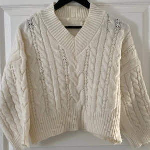 Vit stickad tröja från SHEIN - Supermysig vit stickad tröja från SHEIN med grova flätstickade detaljer och bred ribbad mudd. Tröjan har v-ringad krage och lång ärm, perfekt för lager på lager under kyliga dagar. Oversized fit för en chill vibe.