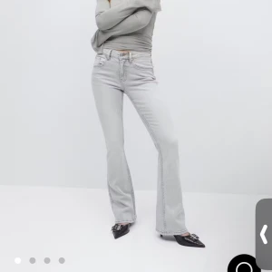 Ljusgrå bootcut med låg midja - Snygga ljusgrå bootcut med låg midja och klassisk femficksdesign. Jeansen har en smal passform och raka ben, tillverkade i mjukt denimtyg med dragkedja och knapp framtill. Perfekta för dig som gillar stilrena och moderna jeans.