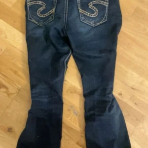 Mörkblå jeans från Silver Jeans Co - Mörkblå jeans med snygga kontrastsömmar och coola bakfickor med broderade detaljer och nitar. Klassisk femficksmodell med låg midja och raka ben. Jeansen är gjorda i slitstarkt denim och har en riktigt schysst tvätt.