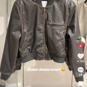 Brun skinn bomberjacka med dragkedja - Snygg brun bomberjacka i skinn med dragkedja framtill, ribbade muddar och fickor med coola detaljer. Jackan har en klassisk bomberform och passar perfekt till streetwear-stilen.