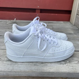 Nike  helvita sneakers - Säljer ett par klassiska Nike Air sneakers i helvitt skinn. Skorna har lågt skaft, rund tå, snörning och perforerade detaljer på tån för extra ventilation. Perfekta för dig som gillar en clean och tidlös look. Använda 2 ggr.