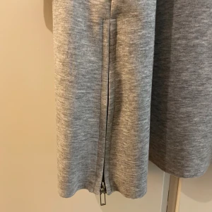 Grå Amisu hoodie/cardigan - Lång, gråmelerad hoodie/cardigan i mjukt material med stora fickor och dragkedjor vid ärmslut och sidor. Köpt från New Yorker. Perfekt för en chill och avslappnad look!