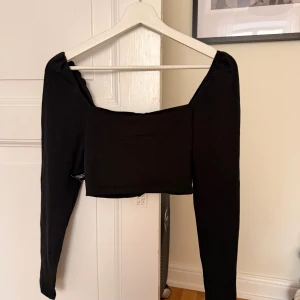 Svart croppad topp från NLY Trend - Svart croppad topp från NLY Trend med långa ärmar och snygg snörning framtill. Toppen har en offshoulder-modell eller om man har det som en vanlig topp och är tillverkad i mjuk bomull. Perfekt för dig som gillar trendiga och stilrena plagg med en twist.