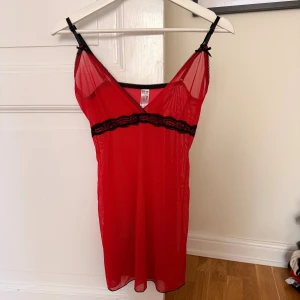 Röd meshklänning med spets  - Röd kort meshklänning/nattklänning från Fashion House med svarta spetsdetaljer under bysten och tunna svarta axelband. Klänningen/nattklänningen är ärmlös och har en lätt transparent look med v-ringning och små rosetter vid axelbanden. Perfekt för dig som vill ha något extra.