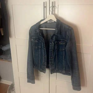 Blå jeansjacka från ONLY, strl 34 - Säljer en klassisk blå jeansjacka från ONLY i storlek 34. Jackan har knappar framtill, två bröstfickor med lock och en snygg tvättad denimlook. Perfekt att slänga över en hoodie eller t-shirt för en chill stil.