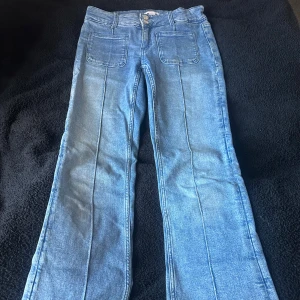 Blå low waist  jeans med bootcut ben från Gina Tricot - Snygga ljusblå jeans från Gina Tricot med bootcut och lågmidjad. Jeansen har två stora framfickor, klassisk bakficka och markerade sömmar längs benen. Stängs med dubbla silverknappar.