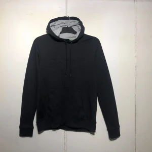 HUGO BOSS Hoodie – Svart (Storlek: Small) - Snygg och stilren hoodie från HUGO BOSS i klassisk svart färg med diskret upphöjd logga framtill. Den är gjord i ett mjukt och bekvämt material som passar perfekt till både vardags och mer avslappnade tillfällen. Insidan av huvan är grå, vilket ger en fin kontrast och extra detalj. Storlek: Small. Skick: Som ny – inga skador, fläckar eller tecken på slitage.  Autentiserad: Äkthetsverifierad.  Passform: Normal/slim fit med klassisk känguruficka och justerbar dragsko i huvan 💸 Cirkapris ny:1200kr