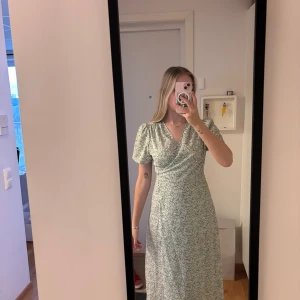 Grön blommig omlottklänning - Snygg lång grön omlottklänning med små vita blommor och knyt i midjan. Klänningen har korta ärmar och v-ringning, perfekt för en fräsch och somrig look. Annonsen finns på flera ställen så skriv till mig innan ni trycker på köp🫶🏻