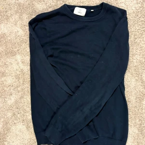 Mörkblå tröja från Bläck, storlek S - En stilren mörkblå tröja från Bläck i storlek S. Tröjan har rund halsringning, långa ärmar och ribbade muddar vid ärmslut och nederkant. Perfekt för lager-på-lager och enkel att matcha med jeans eller chinos.