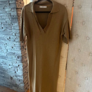 Beige stickad långklänning från MNG - Säljer en beige stickad långklänning från MNG med korta ärmar, v-ringning och krage. Klänningen har en loose passform och är perfekt för dig som gillar en avslappnad men ändå stilren look. Materialet är mjukt och skönt stickat.