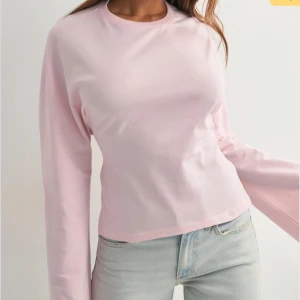 Ljusrosa långärmad topp med knyt - Säljer en ljusrosa långärmad topp i bomull med rund hals och vida ärmar. Toppen är croppad och har en snygg knytning i ryggen som ger en unik look. Perfekt för dig som vill ha något trendigt och bekvämt till våren eller sommaren.