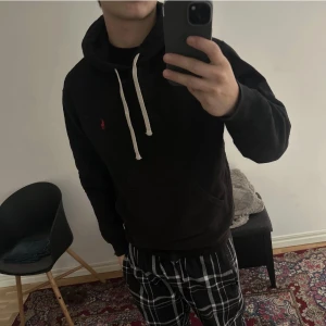  Polo Ralph Lauren hoodie - Svart hoodie från Polo Ralph Lauren med klassisk röd broderad logga på bröstet. Tröjan har huva med vita snören och en stor magficka. Tillverkad i mjuk bomull, perfekt för chill dagar. Snygg och enkel att matcha med allt.