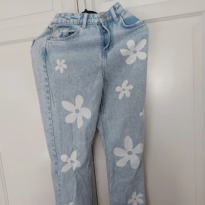 Blommiga ljusblå jeans från FB Sister XXS - ⚠️ Skriv till mig innan köp!⚠️Säljer ett par ljusblå jeans från FB Sister i storlek XXS med vita blommor tryckta över hela byxan. Modellen har klassisk femficksdesign, dragkedja och knapp framtill. Jeansen har en straight passform och är tillverkade i bomull.