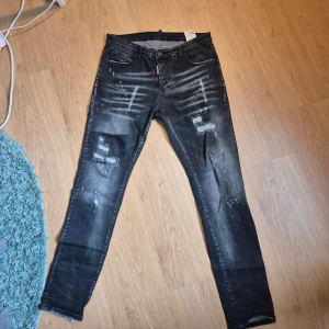  Dsquared2 - Snygga svarta jeans från Dsquared2 med coola slitningar och färgstänk för en edgy look. Jeansen har klassisk femficksmodell, smal passform och tydliga detaljer som Dsquared2-logga på röd etikett och patch bak. Perfekta för dig som gillar streetstyle.