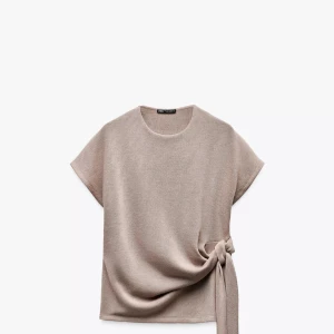 Beige topp med knyt från Zara - Säljer den populära beiga toppen från Zara med rund halsringning och korta ärmar. Toppen har en snygg knytdetalj i sidan som ger en modern touch. 