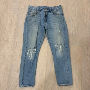 Ljusblå slitna jeans med raka ben - Ljusblå jeans med raka ben och tydliga slitningar och hål på båda knäna. Klassisk femficksmodell med dragkedja och knapp. Jeansen har en avslappnad vibe. 