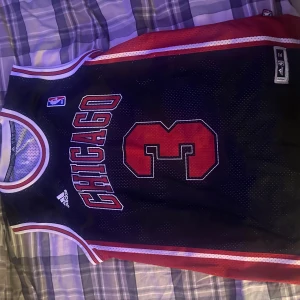 Chicago Bulls Wade baskettröja XL - Snygg Chicago Bulls baskettröja med nummer 3 och Wade på ryggen. Svart mesh-material med röda och vita detaljer, officiell NBA och Adidas-märkning. Perfekt för dig som vill ha en sportig och ikonisk look.