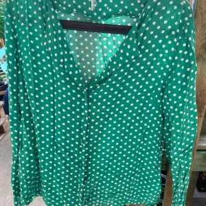 Grön prickig skjorta med knappar - Grön skjorta med vita prickar och knappar framtill. Skjortan har lång ärm och v-ringad halsringning. Perfekt för dig som vill sticka ut med ett lekfullt mönster och fräsch färg.